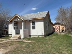 Stucco exterior home featuring a covered front entry with concrete steps, a gable roof with asphalt shingles, and an additional detached shed with a barn-style door. - 