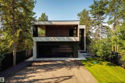 Modern architectural exterior featuring a two-car garage with dark glass panel doors, a second-story balcony with dark railings and wood-panel accents, and an integrated entryway with stone paver steps - 