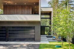 Modern exterior featuring multi-textured facade, a two-car garage with frosted glass doors, a prominent vertical window array, a recessed entry with concrete steps, and a landscaped lawn - 