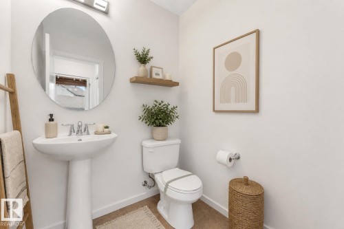 Pedestal sink with chrome faucet, circular wall mirror, and light-toned flooring - 2143 32 Street, Edmonton, AB - Indoor Photo Showing Bathroom