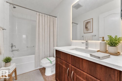 Bathroom featuring a white tub/shower combination with chrome fixtures, a wood-finish vanity with a white countertop, an integrated sink, and an illuminated mirror - 2143 32 Street, Edmonton, AB - Indoor Photo Showing Bathroom