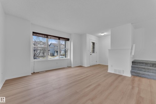 Bright living space featuring expansive windows, wood-finish flooring, a white paneled entry door with decorative glass, a recessed landing, and carpeted stairs - 2143 32 Street, Edmonton, AB - Indoor