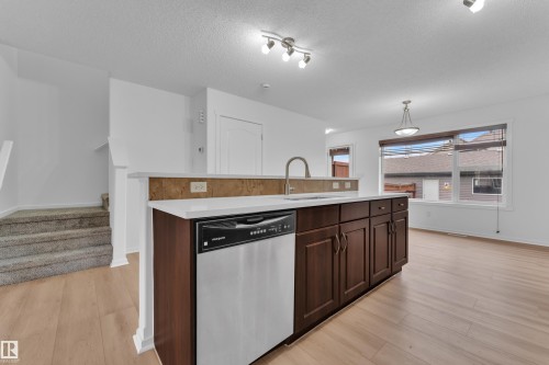 Kitchen island with dark wood-finish cabinetry, a stainless steel dishwasher, and a white countertop - 2143 32 Street, Edmonton, AB - Indoor Photo Showing Kitchen