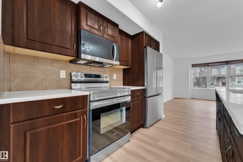 Kitchen featuring dark wood-finish cabinetry, light-toned countertops, tile backsplash, and stainless steel appliances - 2143 32 Street, Edmonton, AB - Indoor Photo Showing Kitchen