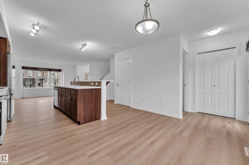 Open-concept kitchen and living area featuring wood-finish flooring, a kitchen island with dark wood cabinetry and light countertops, stainless steel appliances, and a large window with horizontal blinds - 2143 32 Street, Edmonton, AB - Indoor Photo Showing Kitchen