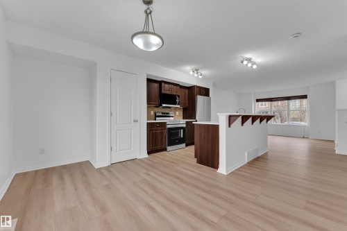 Open-concept living space featuring wood-finish flooring, a kitchen island with seating, dark wood cabinetry, and stainless steel appliances - 2143 32 Street, Edmonton, AB - Indoor Photo Showing Kitchen
