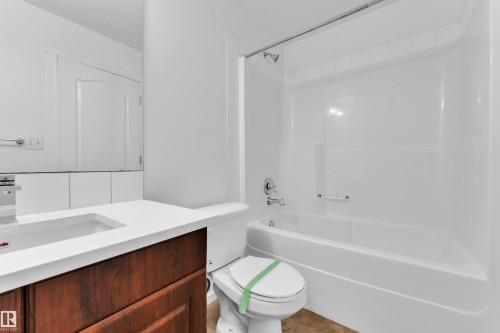 Bathroom featuring a white bathtub and shower combination, a built-in wood-finish vanity with a white countertop, an integrated sink, and a mirrored wall - 2143 32 Street, Edmonton, AB - Indoor Photo Showing Bathroom