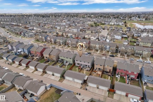Residential neighborhood featuring detached and attached multi-story homes, individual garages, and a communal green space with a water feature - 2143 32 Street, Edmonton, AB - Outdoor With View