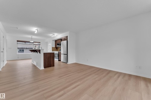 Expansive living area featuring light wood-finish flooring, a kitchen with stainless steel appliances, dark wood cabinetry, a breakfast bar, and recessed lighting - 2143 32 Street, Edmonton, AB - Indoor