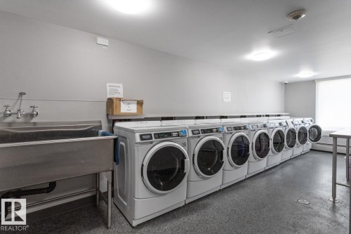 On-site laundry facility featuring multiple front-loading washers, complementing dryer & a large utility sink. - 602 12303 Jasper Avenue, Edmonton, AB - Indoor Photo Showing Laundry Room