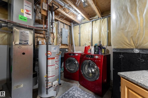 Dedicated utility area featuring a water heater, furnace, electrical panel, exposed ceiling joists, and a partial built-in cabinet with a granite-finish countertop - 2 13403 Cumberland Road, Edmonton, AB - Indoor Photo Showing Laundry Room