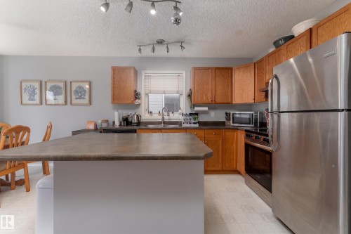 Kitchen featuring a central island with a solid surface countertop, wood cabinetry, stainless steel appliances, and a window above the sink - 2 13403 Cumberland Road, Edmonton, AB - Indoor Photo Showing Kitchen With Stainless Steel Kitchen