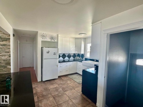 Kitchen featuring white cabinetry, a farmhouse-style sink, and a black and white geometric tile backsplash - 8620 137 Avenue, Edmonton, AB - Indoor