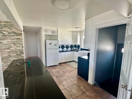 Kitchen featuring white cabinetry, black and white diamond-patterned backsplash, dark countertops, and tile flooring - 8620 137 Avenue, Edmonton, AB - Indoor
