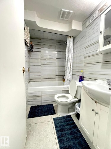 Bathroom featuring floor-to-ceiling horizontally striped wall tile, a white bathtub, and a white toilet - 8620 137 Avenue, Edmonton, AB - Indoor Photo Showing Bathroom