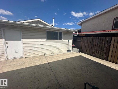 Concrete patio area featuring a white exterior door, a horizontal sliding window, light-toned horizontal siding, and a wooden fence - 8620 137 Avenue, Edmonton, AB - Outdoor With Exterior