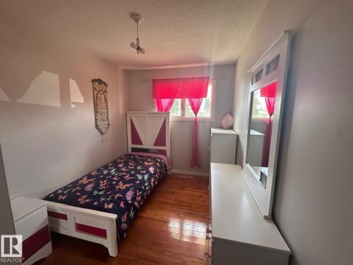 Interior room with wood-finish flooring, light grey walls, and a window with red curtains - 8620 137 Avenue, Edmonton, AB - Indoor Photo Showing Bedroom