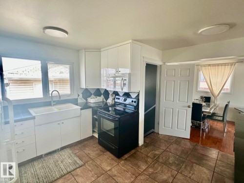 Kitchen featuring a double basin farmhouse sink with a gooseneck faucet, black and white diamond pattern backsplash, white cabinetry, and a black range - 8620 137 Avenue, Edmonton, AB - Indoor Photo Showing Kitchen