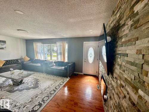 Living area featuring a stone veneer accent wall, wood-finish flooring, and recessed ceiling lighting - 8620 137 Avenue, Edmonton, AB - Indoor
