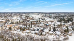The property is situated within a community featuring various residential buildings and abundant mature trees, with a clear sky overhead - 