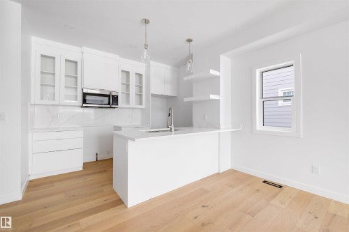 The kitchen features a white island with a sink, white cabinetry, and a microwave - 7927 112S Avenue, Edmonton, AB - Indoor Photo Showing Kitchen