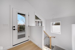 Entryway featuring light-toned flooring, a full-view glass door with black hardware, and a staircase with a natural wood handrail and black balusters - 