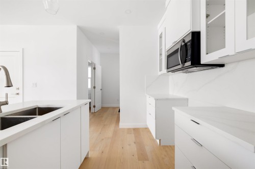 The kitchen features light wood flooring, white cabinetry, a double basin sink with a modern faucet, and a built-in microwave oven - 7927 112S Avenue, Edmonton, AB - Indoor Photo Showing Kitchen With Double Sink