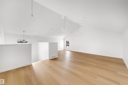 Spacious room featuring light wood flooring, white walls, and a vaulted ceiling with pendant lighting - 