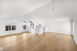 Spacious open-concept room featuring light wood flooring, vaulted white ceilings with recessed lighting, and large windows providing natural light - 