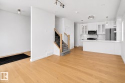 Open concept living area featuring light wood-finish flooring, a contemporary kitchen, and a staircase with wood handrails and black metal balusters - 