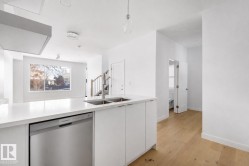 Contemporary kitchen featuring an island with a double stainless steel sink, integrated dishwasher, and white cabinetry - 
