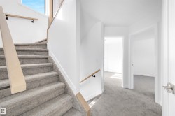 The property features a staircase with carpeted steps and a light-colored wooden handrail, leading to an upper landing with light gray carpet and white walls - 