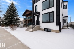Modern exterior featuring white siding with black trim, large black-framed windows, and a concrete staircase with black metal railings - 