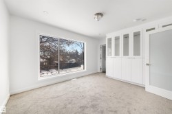 This room features a large window, light-colored carpeting, and a built-in white storage unit with glass-fronted upper cabinets - 