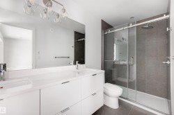 Bathroom featuring a spacious double vanity with white cabinets, a large mirror, and an enclosed shower with dark tile surround and a rain shower head - 
