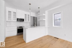 Contemporary kitchen featuring a center island, stainless steel appliances, white cabinetry, integrated sink, and wood-finish flooring - 