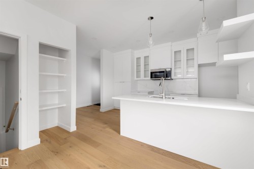 Open concept kitchen and living area featuring light wood flooring, white cabinetry, a kitchen island with an integrated sink, and stainless steel appliances - 7927 112S Avenue, Edmonton, AB - Indoor Photo Showing Kitchen With Double Sink