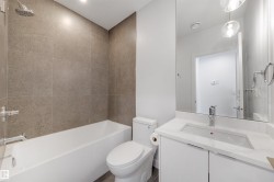Bathroom with a white bathtub, a toilet, a vanity with a white countertop and integrated sink, a large mirror, and tiled walls in the shower area - 