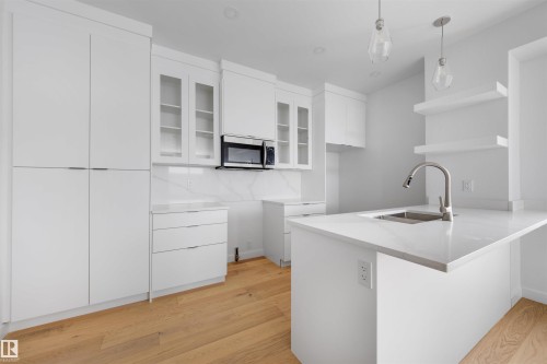 The kitchen features light wood flooring, white cabinetry, a kitchen island with an integrated sink, and white countertops - 7927 112S Avenue, Edmonton, AB - Indoor Photo Showing Kitchen With Upgraded Kitchen