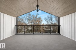 Covered balcony featuring a wood-finish vaulted ceiling, board and batten siding, a black metal and glass railing, and a contemporary hanging light fixture - 