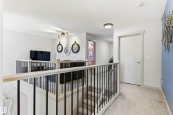 Upper-level landing with light-toned carpeting, modern black metal and light wood railing, recessed lighting. - 