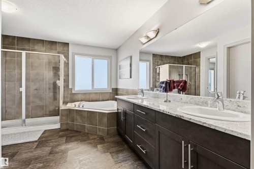 Bathroom featuring a full-width mirror, granite top vanity with two sinks, and a large soaker tub. - 7343 Armour Crescent, Edmonton, AB - Indoor Photo Showing Bathroom