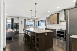 Open-concept interior featuring dark wood-finish flooring throughout, a central kitchen island with seating, stainless steel appliances, and a tiled kitchen backsplash - 