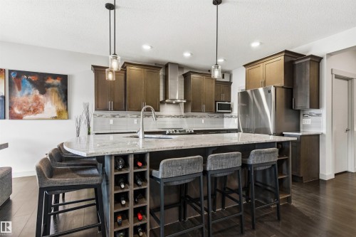 Spacious kitchen featuring an oversized island with a built-in wine rack, stone countertop, and integrated sink - 7343 Armour Crescent, Edmonton, AB - Indoor