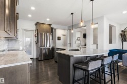 Kitchen featuring an expansive island with a built-in sink, stainless steel appliances, wood-finish flooring, a tile backsplash, and recessed lighting - 