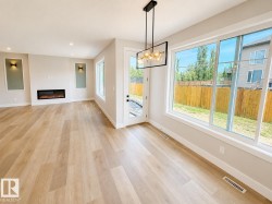 Open-concept living space featuring wood-finish flooring, a linear electric fireplace, and expansive windows - 
