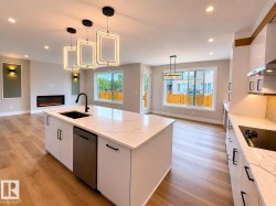 Open-concept kitchen featuring a large island with a black sink and matte black faucet, integrated dishwasher, and white quartz countertops - 