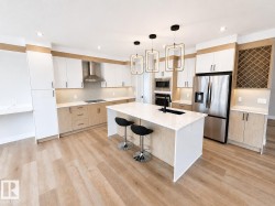 Modern kitchen featuring a large central island with seating, stainless steel appliances, two-tone cabinetry, and wood-finish flooring - 