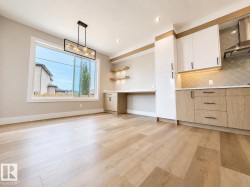 Open-concept living area featuring light wood-finish flooring, a large picture window, and a linear chandelier - 