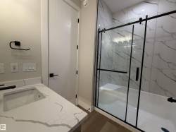Contemporary bathroom featuring a spacious walk-in shower with black-framed glass doors and white marbled wall tiles - 